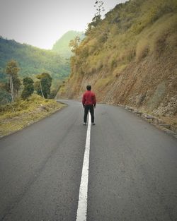 Rear view of young man standing on road against mountain