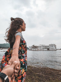 Cropped man holding woman hand standing by lake