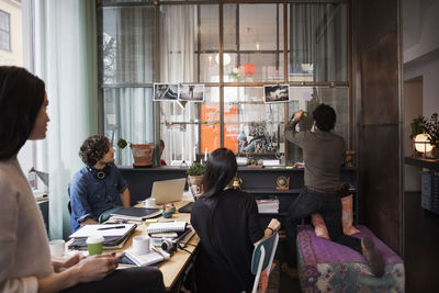 Colleagues looking at man sticking adhesive note on glass at creative office