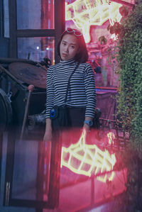 Portrait of young woman standing against illuminated built structure