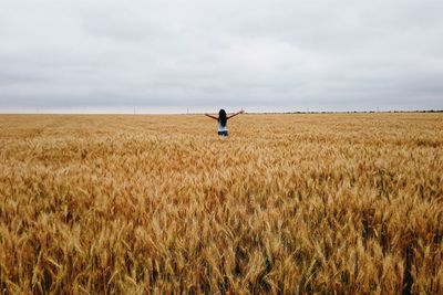 Rear view of woman standing on field against cloudy sky