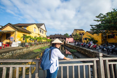 Portrait of woman standing by railing on bridge against buildings