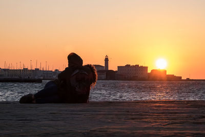 Rear view of couple romancing in front of sea at sunset