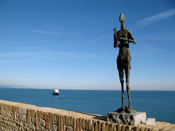 Statue by sea against blue sky