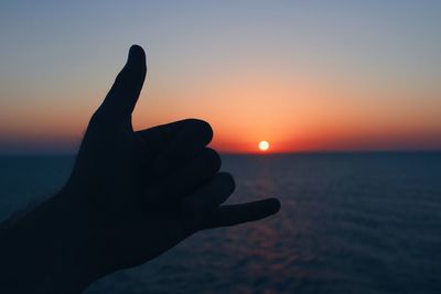 Close-up of silhouette hand against sea during sunset