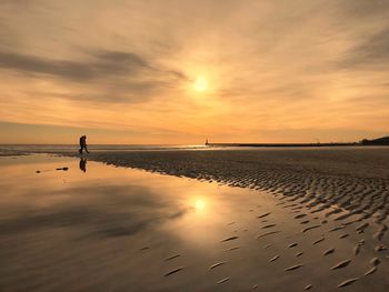 Silhouette friends walking at beach against sky during sunset