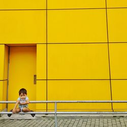 Boy hanging on railing against yellow building
