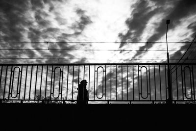 Silhouette man standing on bridge against cloudy sky