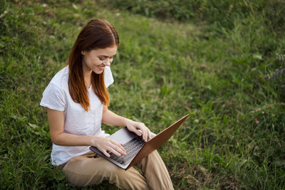 Young woman using laptop while sitting on field