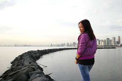 Rear view of smiling woman standing at beach against cityscape