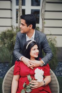 Thoughtful man with happy pregnant girlfriend sitting on chair