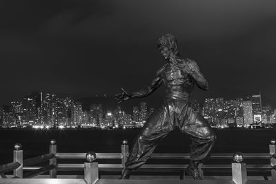 Statue against illuminated buildings in city at night