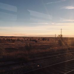 Railroad track on field against sky during sunset