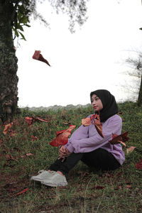Young man sitting on field against sky