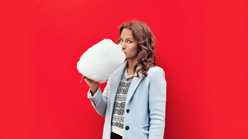 Portrait of woman eating cotton candy while standing against red background
