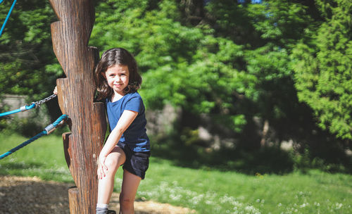 Caucasian beautiful girl hangs on a wooden pole from a rope swing in a park on a playground