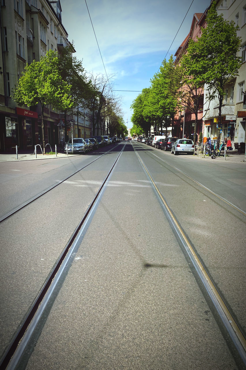 lane, road, architecture, street, city, transportation, building exterior, built structure, road surface, sky, tree, infrastructure, urban area, nature, mode of transportation, plant, neighbourhood, city street, residential area, car, sign, the way forward, motor vehicle, day, diminishing perspective, building, city life, asphalt, symbol, road marking, vanishing point, cloud, outdoors, residential district, no people, transport, vehicle, marking, tarmac, suburb