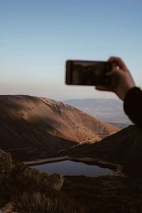 Man photographing through smart phone against sky