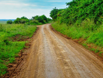 Dirt road amidst field against sky