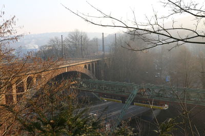 Bridge over bare trees against sky