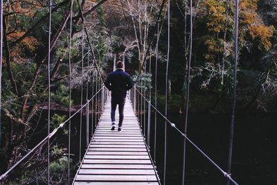 Rear view of man on footbridge in forest