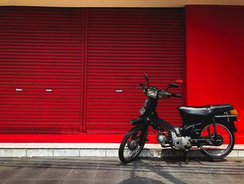 Motorcycle parked on footpath against red shutter