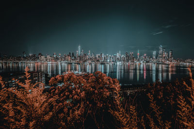 Illuminated buildings by sea against sky at night