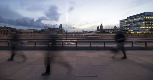 Blurred motion of people walking on bridge in city against sky