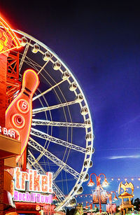 Low angle view of illuminated ferris wheel against blue sky