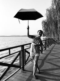 Woman dancing with umbrella by railing against sea and sky