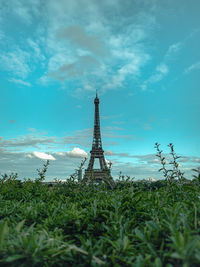 View of eiffel tower on field against cloudy sky