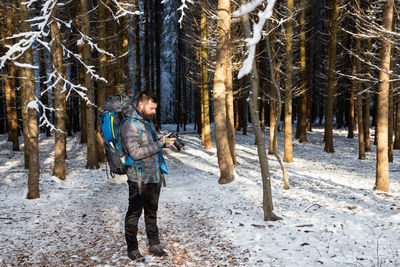 Man standing amidst trees in forest during winter