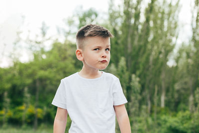 Boy looking away while standing against trees