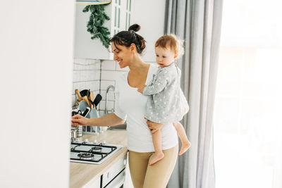 Smiling mother with daughter standing in kitchen