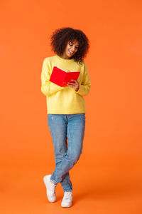 Full length of smiling woman reading book standing against colored background