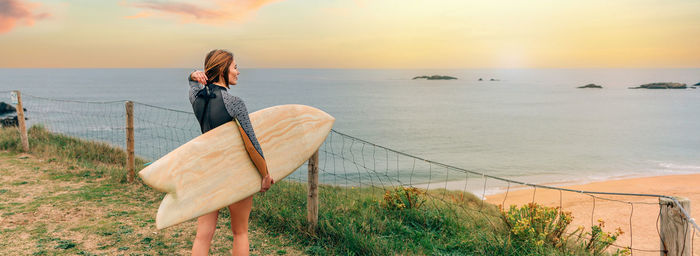 Surfer woman putting her hair up while looking at the beach from the shore