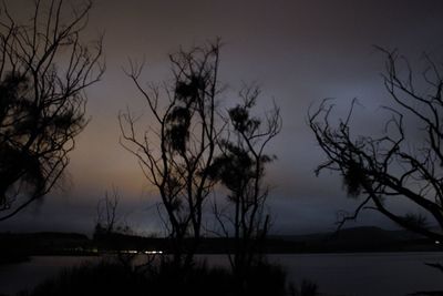 Silhouette bare trees by lake against sky at sunset