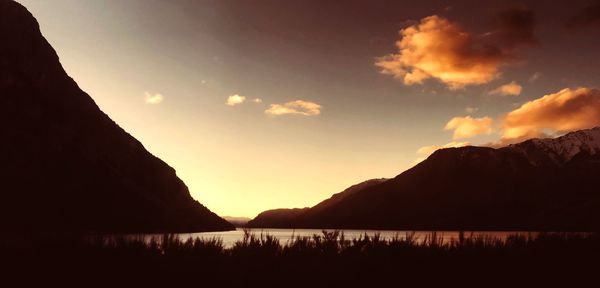 Scenic view of lake by silhouette mountains against sky during sunset