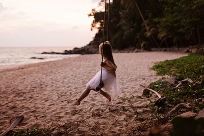 Girl sitting on swing at beach during sunset