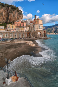 Buildings by sea against cloudy sky