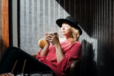 Woman sitting in a cafe holding a warm drink enjoying the sunshine