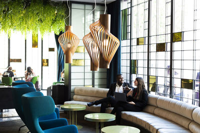 Multi-ethnic male and female colleagues discussing while sitting on sofa in modern bar