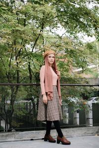 Woman looking away while standing against railing and trees