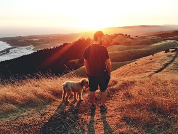 Rear view of man standing with dog on hill during sunset