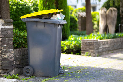 Full garbage trash can standing at sidewalk next to street waiting to get collected and empty