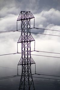 Low angle view of electricity pylon against cloudy sky