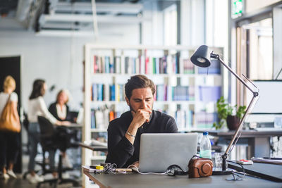 Worried businessman with hand on chin looking at laptop while sitting in office