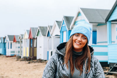 Portrait of smiling young woman standing at beach against sky