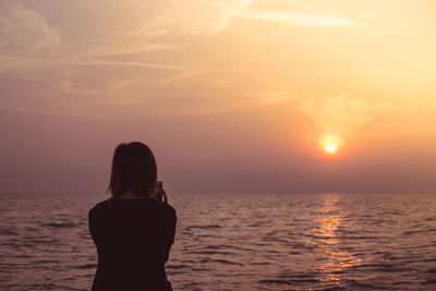 Rear view of silhouette woman standing at beach during sunset