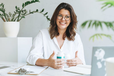 Young smiling brunette woman nutritionist plus size in white shirt working at laptop on table 